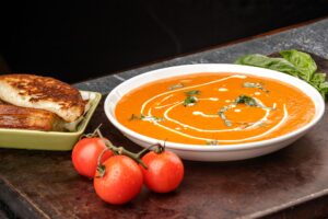 A delicious bowl of Tomato Basil Bisque Soup with a Grilled Cheese Sandwich on the side.