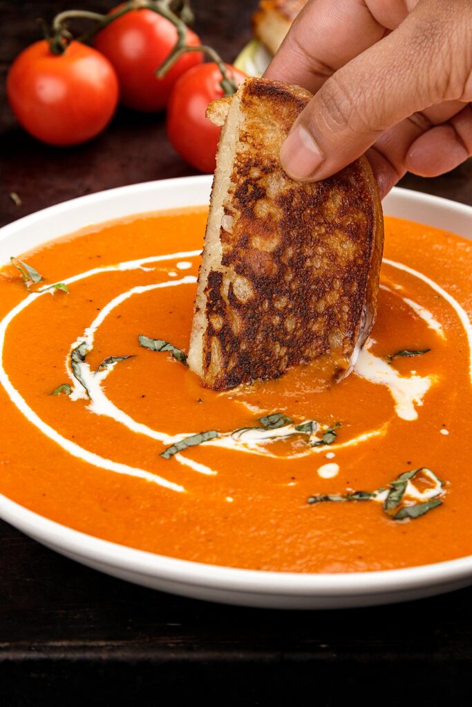 A grilled provolone cheese sourdough sandwich dipped into a bowl of tomato basil bisque soup