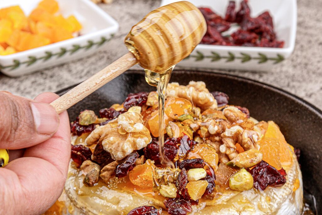 Baked brie topped with nuts, dried fruits and apricot jam. Drizzled with honey